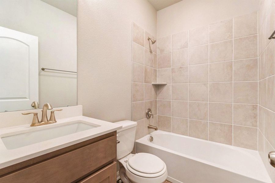 This is a modern bathroom featuring a sleek vanity with a white countertop and brass fixtures. It includes a bathtub with a tiled shower surround and a neutral color scheme, offering a clean and inviting space.