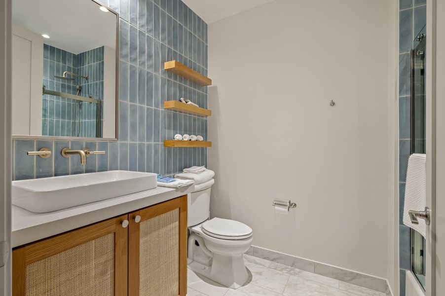 A fresh bathroom features a modern vanity with a vessel sink and stylish blue tile accents.