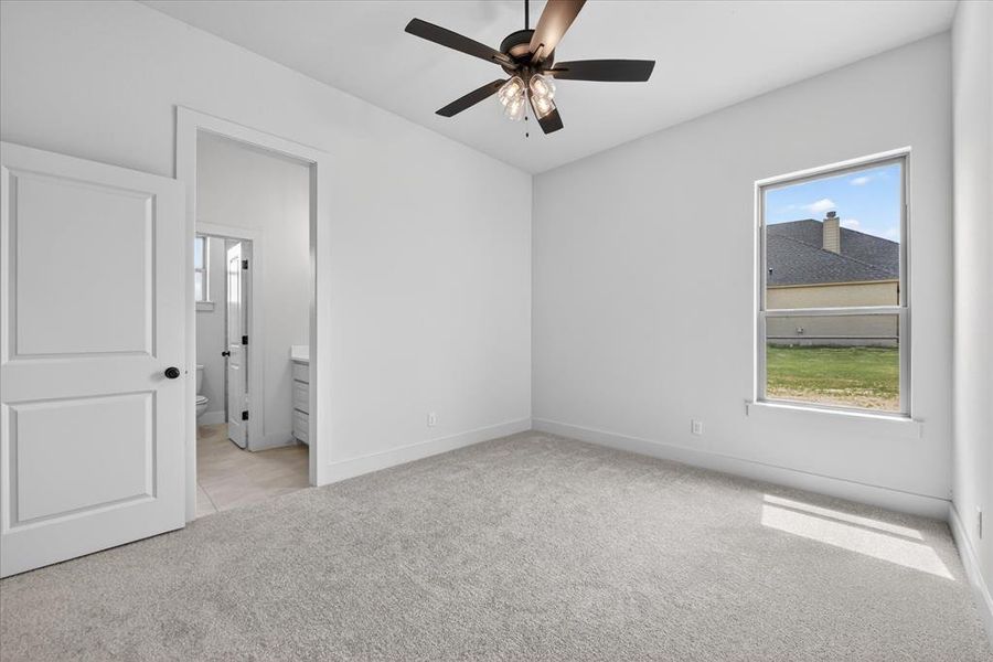 Unfurnished bedroom featuring light colored carpet, ceiling fan, and ensuite bath