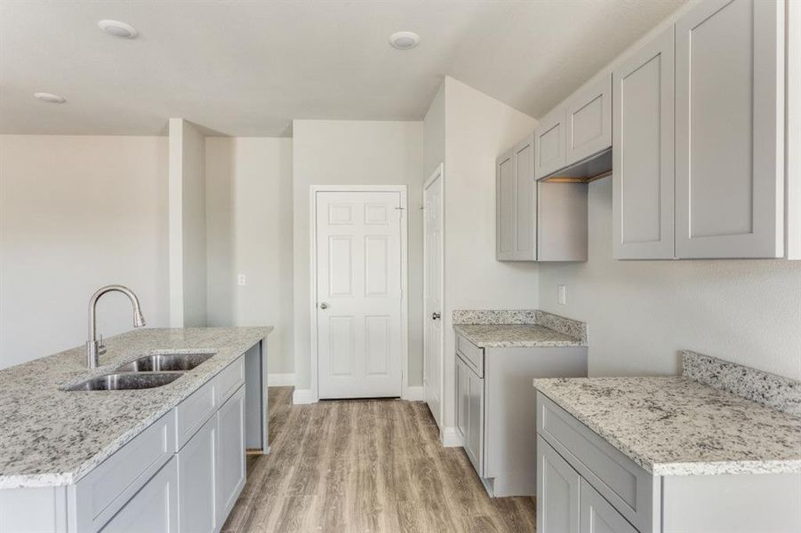 Kitchen featuring gray cabinets, light wood-type flooring, light stone countertops, and a center island with sink