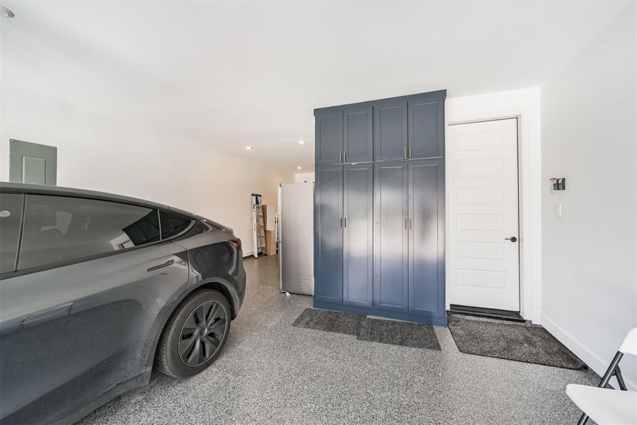 A spacious three-car garage featuring durable epoxy flooring and custom floor-to-ceiling cabinets designed exclusively for storage. A spacious three-car garage featuring durable epoxy flooring and custom floor-to-ceiling cabinets designed exclusively for storage.