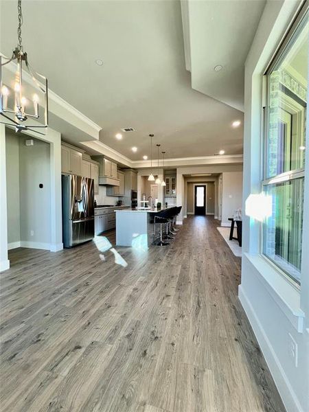 View from breakfast area to your kitchen with contemporary gray cabinetry, beautiful transitional taste granite counter tops, massive island with a sink for food prep, serving that fits 4 bar stools, easy to clean luxury plank style flooring, all open to the family room. Great for entertaining and hosting holiday parties.