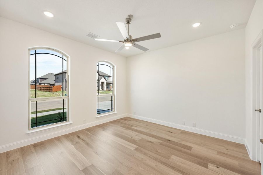 Empty bedroom with light wood floors, ceiling fan, and two arched windows overlooking a neighborhood Empty bedroom with light wood floors, ceiling fan, and two arched windows overlooking a neighborhood
