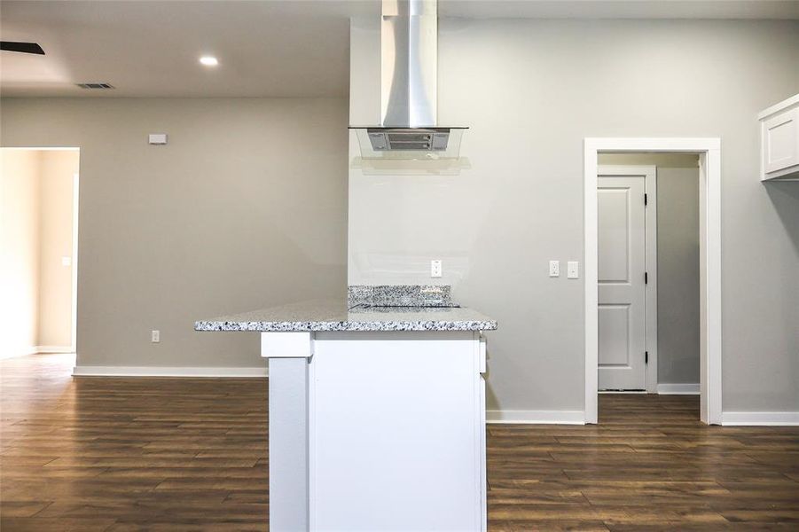 Kitchen featuring dark wood-style flooring, light stone counters, wall chimney range hood, recessed lighting, and white cabinets Kitchen featuring dark wood-style flooring, light stone counters, wall chimney range hood, recessed lighting, and white cabinets