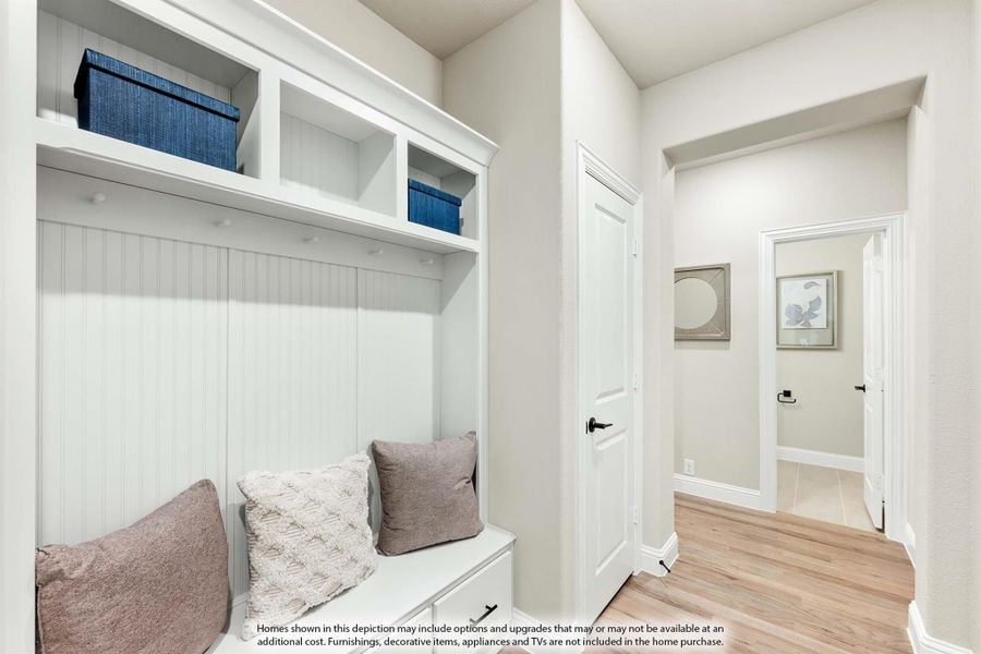 Mudroom with white built-in bench, upper storage cubbies, coat hooks, and beadboard paneling on light hardwood floors Mudroom with white built-in bench, upper storage cubbies, coat hooks, and beadboard paneling on light hardwood floors