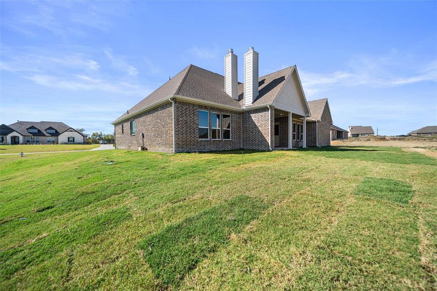 Rear view of property featuring a lawn, a patio area, brick siding, a shingled roof, and a chimney Rear view of property featuring a lawn, a patio area, brick siding, a shingled roof, and a chimney