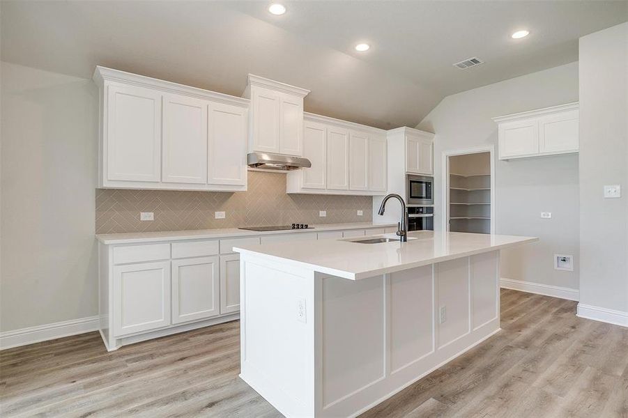 Kitchen featuring white cabinetry, stainless steel appliances, ventilation hood, an island with sink, and light wood-type flooring