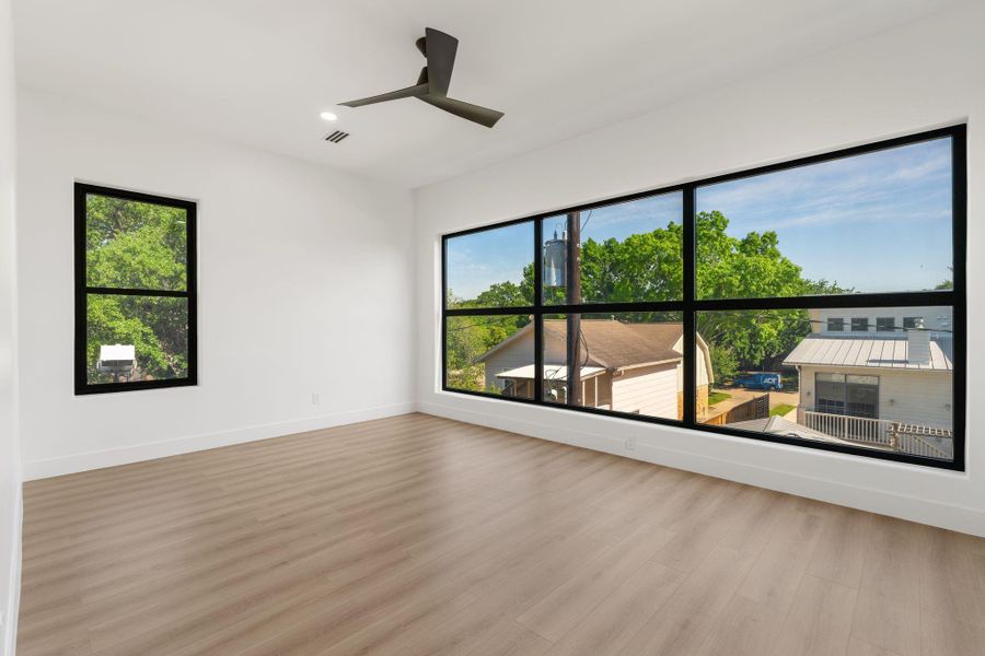 Floor-to-ceiling multi-panel black-framed windows dominate the far wall of this secondary bedroom — an extraordinary amount of natural light for a bedroom, with an elevated treetop view that makes the most of every inch of glass.