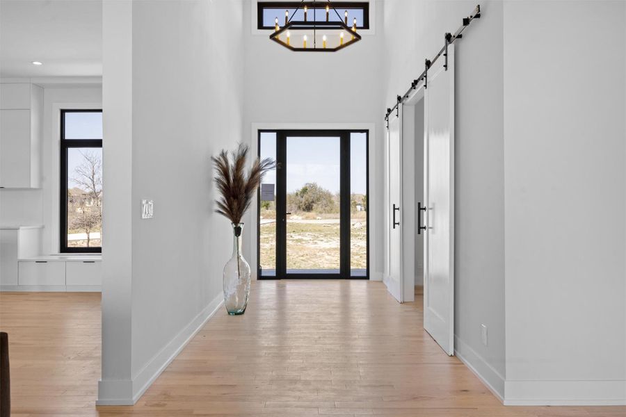 Open space foyer with a chandelier, a barn door, light wood finished floors, baseboards, and a towering ceiling