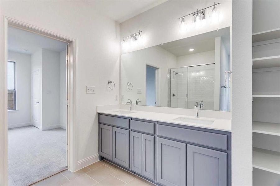 Bathroom featuring a stall shower, tile patterned flooring, double vanity, and baseboards