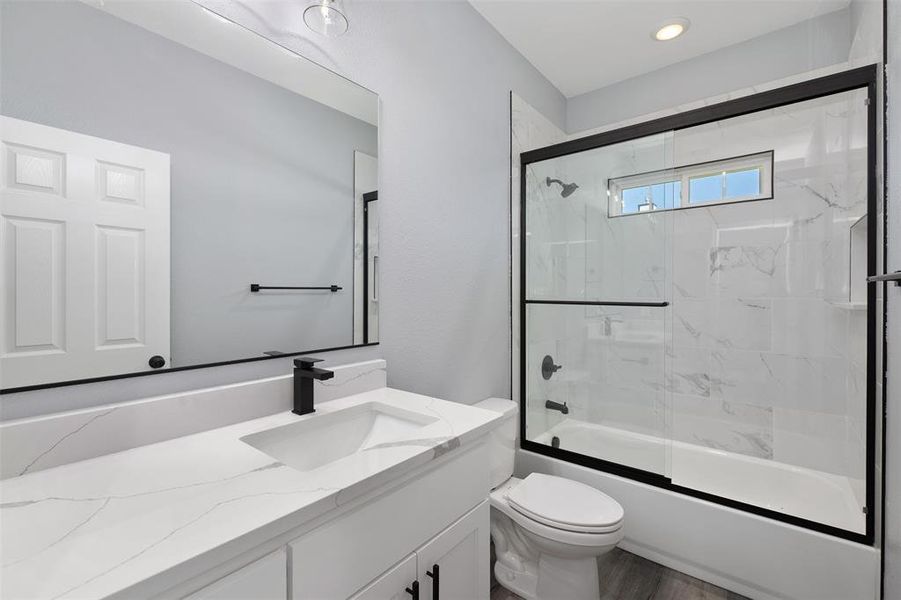 Bathroom with vanity, bath / shower combo with glass door, and wood finished floors Bathroom with vanity, bath / shower combo with glass door, and wood finished floors