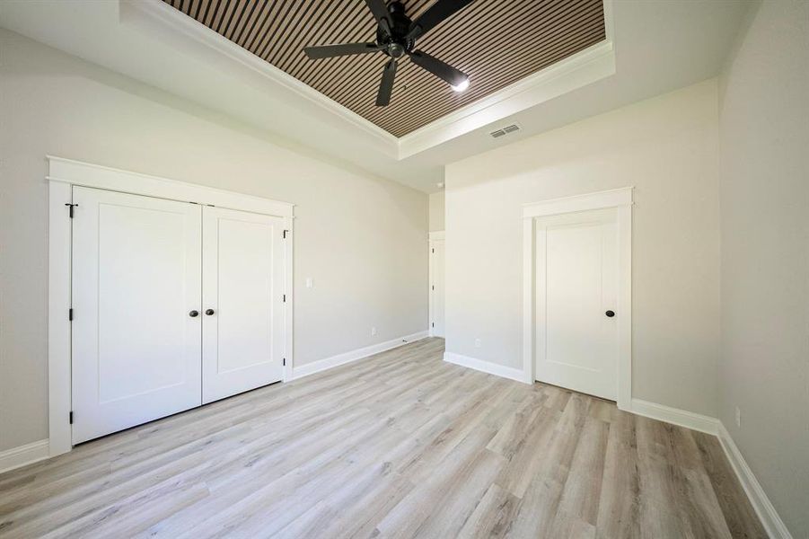Unfurnished bedroom with a tray ceiling, light wood-style flooring, a closet, and ceiling fan Unfurnished bedroom with a tray ceiling, light wood-style flooring, a closet, and ceiling fan