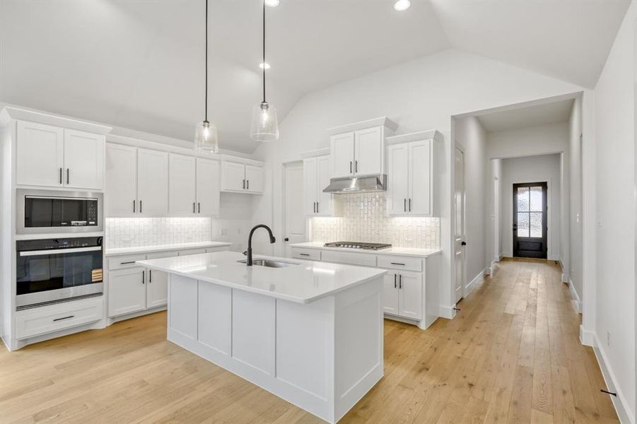 Kitchen with stainless steel appliances, white cabinetry, backsplash, and vaulted ceiling