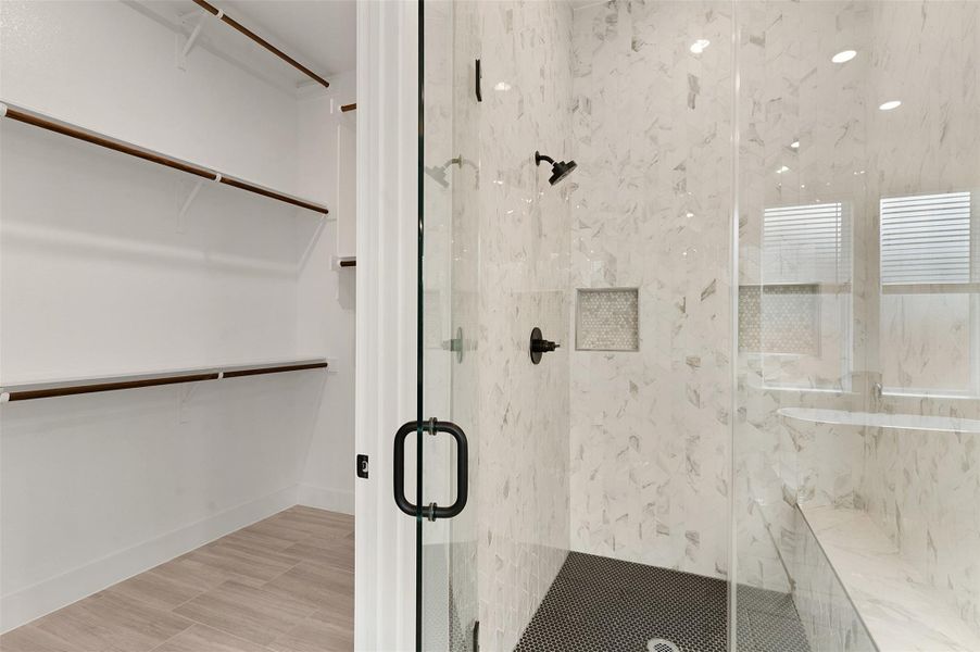 Full bath featuring a marble finish shower, a walk in closet, and light wood-style floors Full bath featuring a marble finish shower, a walk in closet, and light wood-style floors