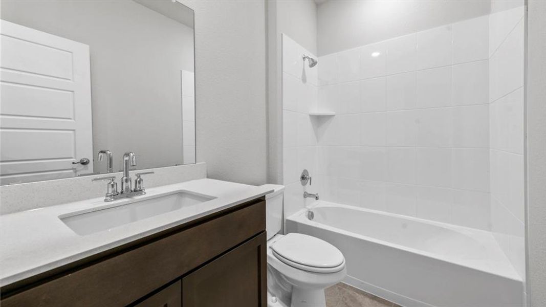 Bathroom featuring a white subway tile shower surround, integrated bathtub, and a dark wood-finish vanity with a white countertop and undermount sink