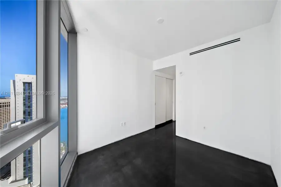 Floor-to-ceiling windows featuring urban scenery, polished concrete flooring, white walls, and interior sliding closet doors Floor-to-ceiling windows featuring urban scenery, polished concrete flooring, white walls, and interior sliding closet doors