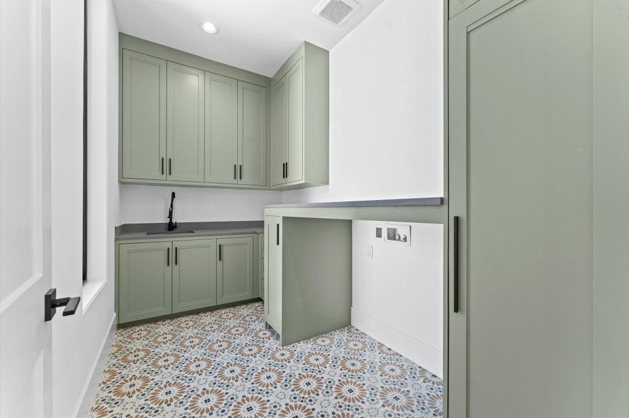 This laundry room features elegant green cabinetry, a sleek black faucet, and stylish patterned tile flooring. It's a functional and modern space for your laundry needs.