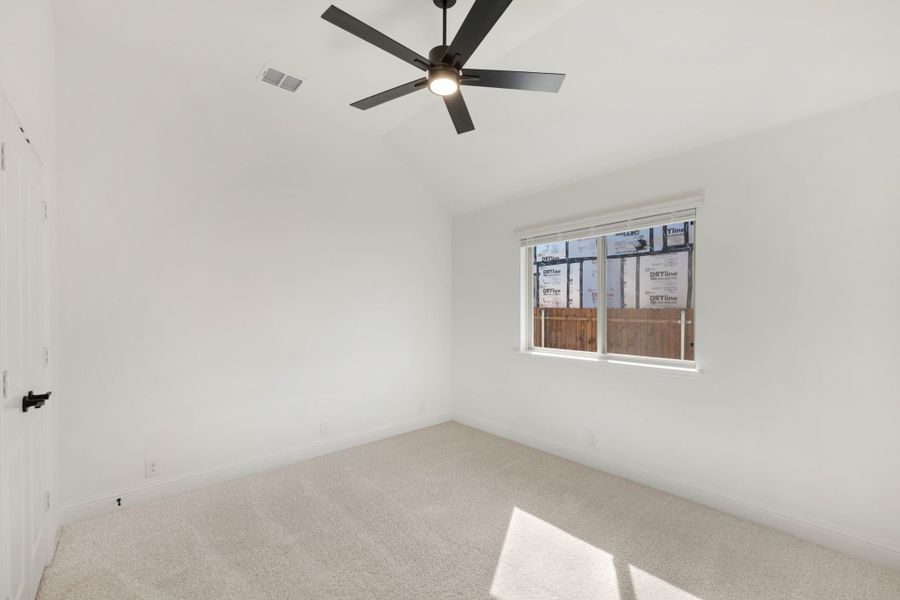 Empty bedroom with carpet flooring, vaulted ceiling, ceiling fan, and a single window with white walls.