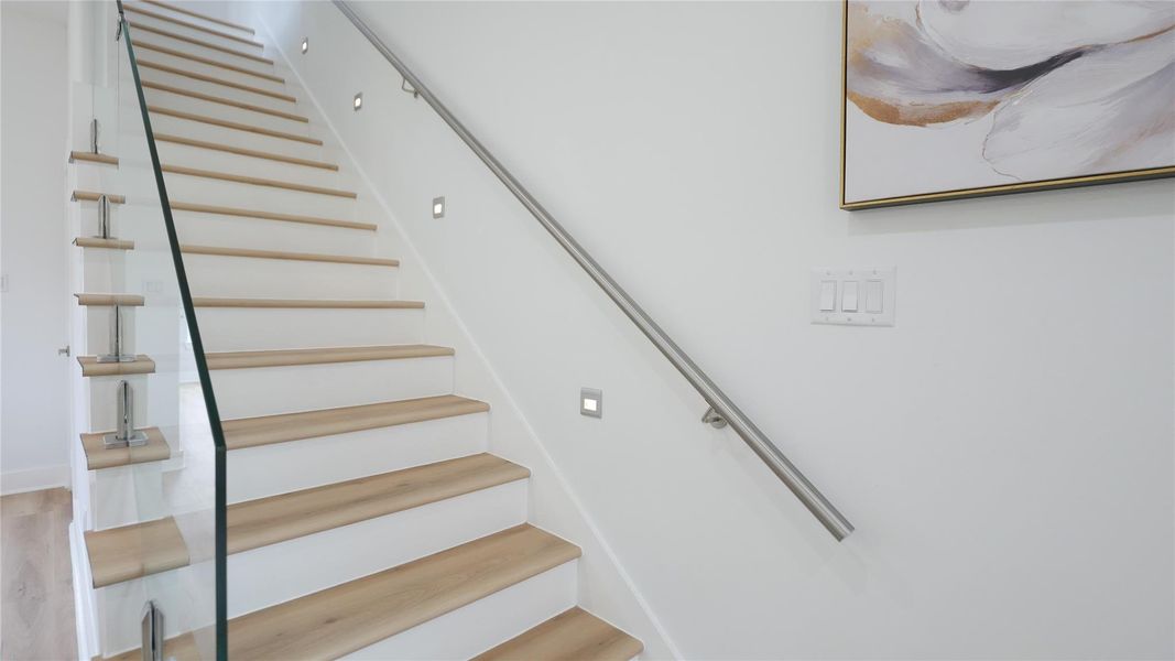 This photo showcases a modern staircase with light wood steps, sleek glass railing, and integrated wall lighting, set against a clean white wall. This photo showcases a modern staircase with light wood steps, sleek glass railing, and integrated wall lighting, set against a clean white wall.