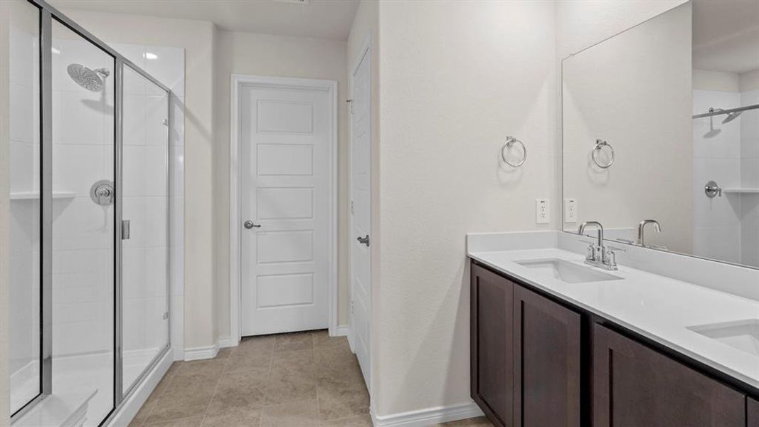 Bathroom featuring a glass-enclosed shower with a rainfall showerhead, a double vanity with a light-colored countertop, dark wood-finish cabinetry, and a large wall-mounted mirror