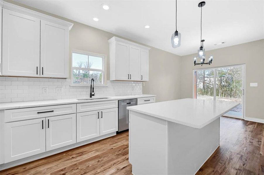 Kitchen featuring stainless steel dishwasher, sink, pendant lighting, light hardwood / wood-style flooring, and white cabinets