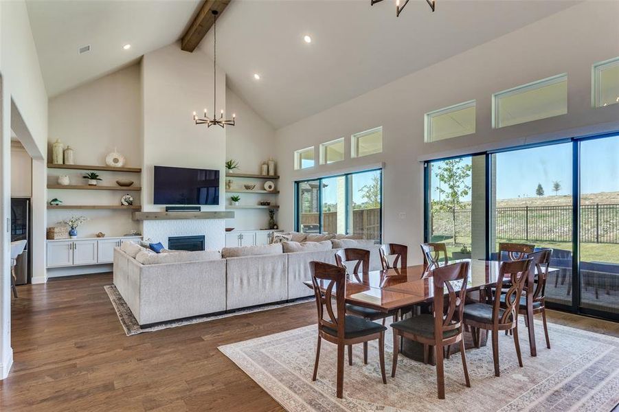 Dining area with a chandelier, high vaulted ceiling, a fireplace, beam ceiling, and dark wood-style flooring Dining area with a chandelier, high vaulted ceiling, a fireplace, beam ceiling, and dark wood-style flooring