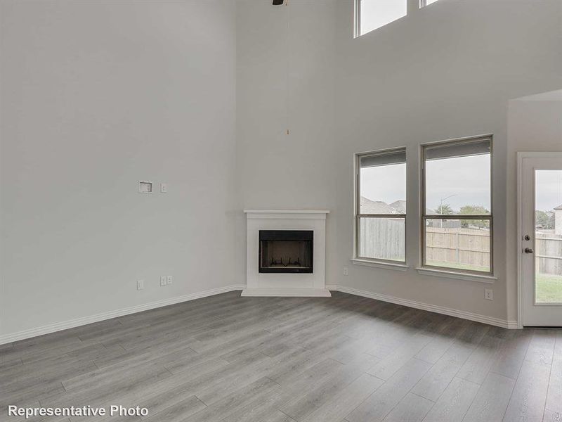 Unfurnished living room featuring a fireplace with raised hearth, light wood finished floors, and a towering ceiling
