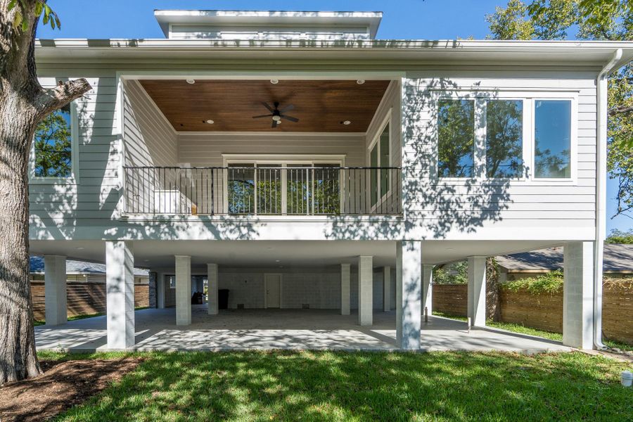 Elevated two-story home with open ground level for parking or storage, plus a covered deck above with a ceiling fan and sliding glass doors overlooking the landscaped yard. Elevated two-story home with open ground level for parking or storage, plus a covered deck above with a ceiling fan and sliding glass doors overlooking the landscaped yard.