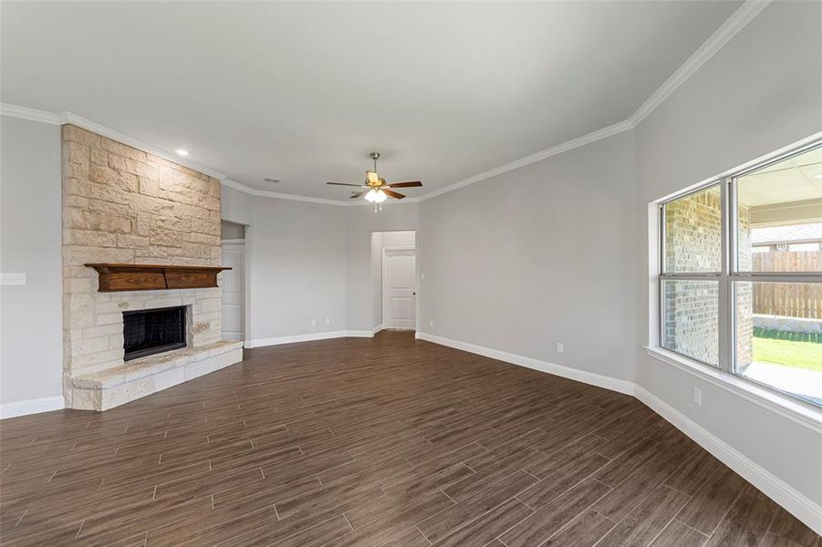 Unfurnished living room with ceiling fan, a stone fireplace, ornamental molding, and dark wood-type flooring