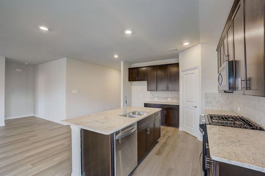 Kitchen featuring stainless steel appliances, sink, light hardwood / wood-style flooring, backsplash, and a kitchen island with sink