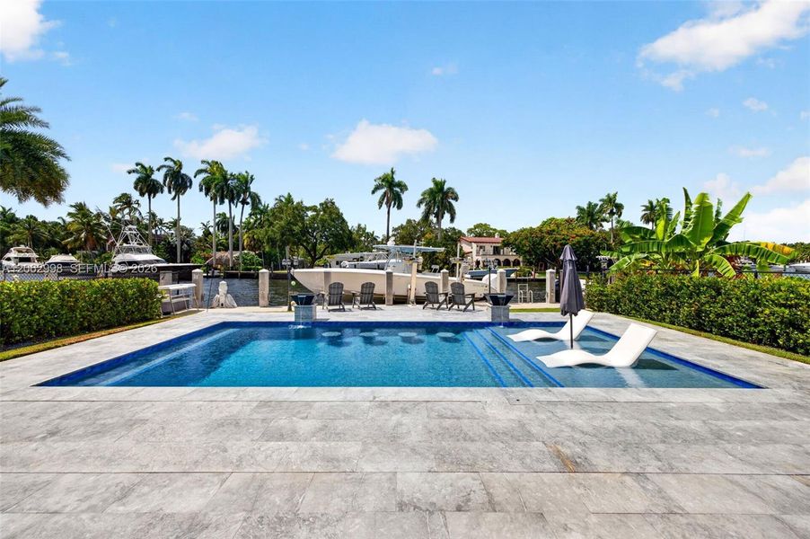 Salt chlorinated pool w/ water features, LED color changing light, sun shelf with umbrella hole and in water stools. Stone decking surrounds the pool
