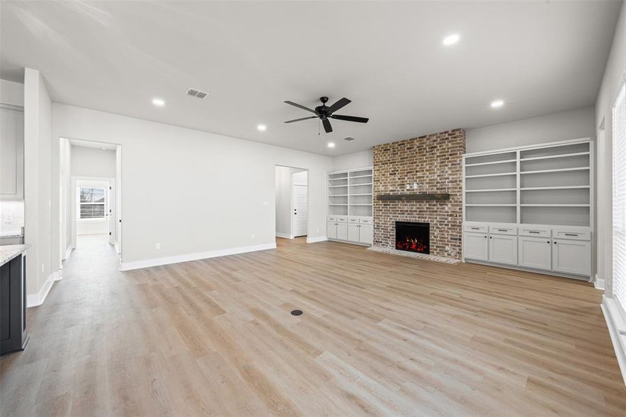 Unfurnished living room with a fireplace, light wood-style flooring, recessed lighting, a ceiling fan, and built in shelves Unfurnished living room with a fireplace, light wood-style flooring, recessed lighting, a ceiling fan, and built in shelves
