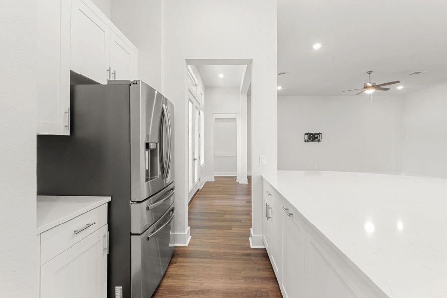 Kitchen featuring stainless steel fridge with ice dispenser, light countertops, dark wood-type flooring, ceiling fan, and white cabinets Kitchen featuring stainless steel fridge with ice dispenser, light countertops, dark wood-type flooring, ceiling fan, and white cabinets