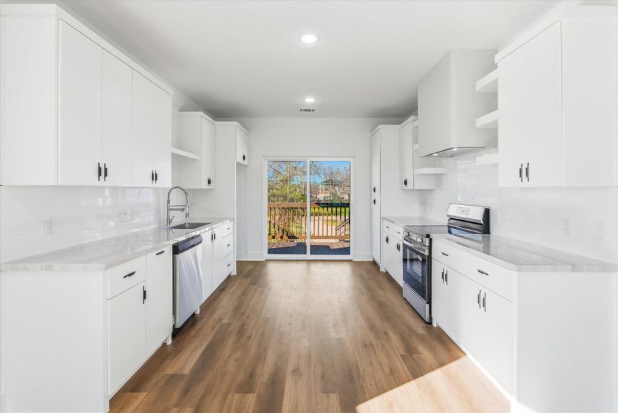 Spacious galley kitchen featuring custom solid-wood cabinetry with soft-close drawers and hinges, a custom stucco vent hood, and a stainless steel stove.