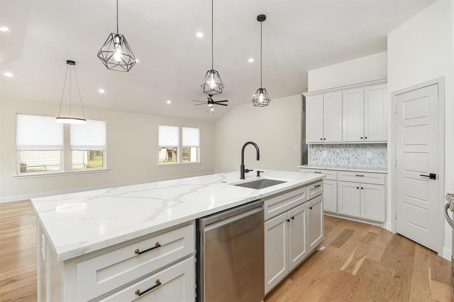 Kitchen featuring backsplash, dishwasher, light wood-style flooring, white cabinets, and a sink