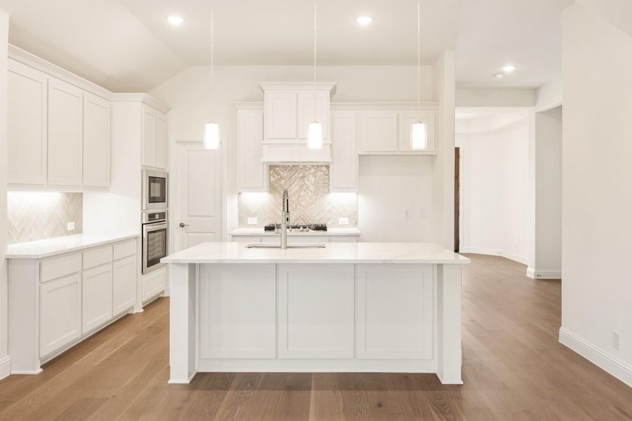 White kitchen with large center island, pendant lights, herringbone backsplash, and hardwood floors White kitchen with large center island, pendant lights, herringbone backsplash, and hardwood floors
