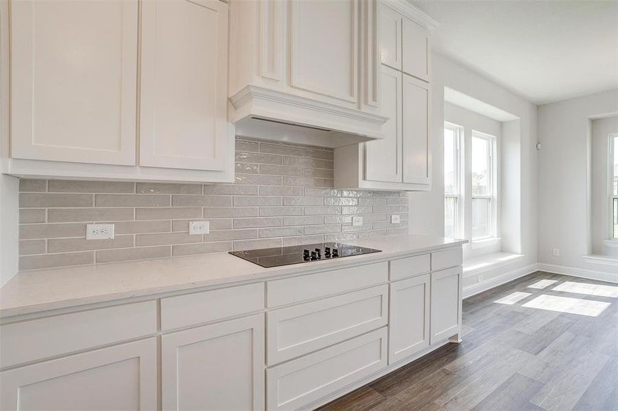 Kitchen featuring hardwood / wood-style floors, black electric cooktop, tasteful backsplash, white cabinets, and custom exhaust hood