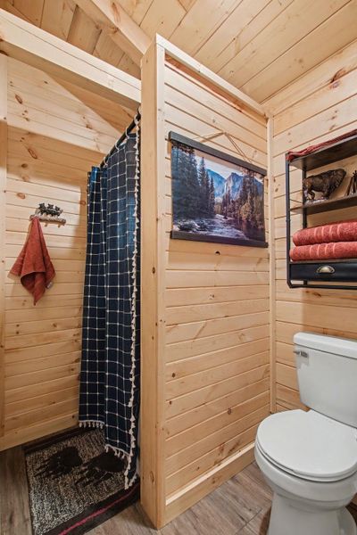 Full bathroom with wooden walls, a shower with shower curtain, light wood-type flooring, and wood ceiling