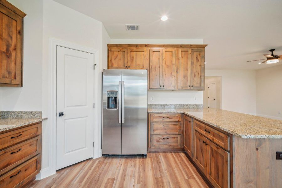 Kitchen with visible vents, light wood-style flooring, a ceiling fan, stainless steel refrigerator with ice dispenser, and a peninsula