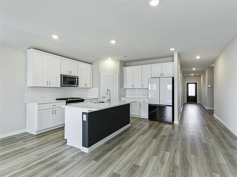 Kitchen with a kitchen island with sink, sink, fridge, white cabinetry, and range