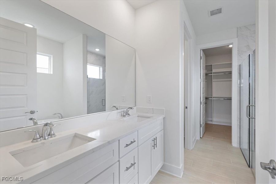 Bathroom with a spacious closet, a marble finish shower, and double vanity