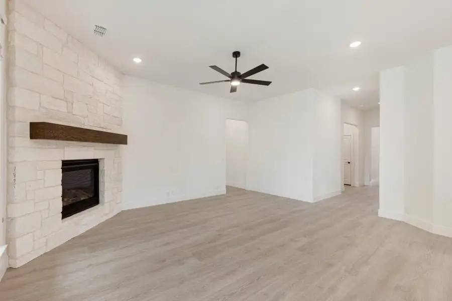 Open living room with stone fireplace, wood mantel, ceiling fan, and light hardwood floors