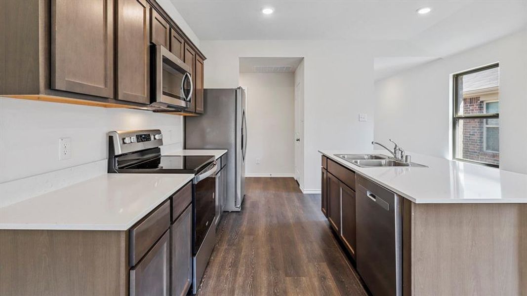 Kitchen with a center island with sink, stainless steel appliances, dark wood-type flooring, recessed lighting, and dark wood finish cabinetry Kitchen with a center island with sink, stainless steel appliances, dark wood-type flooring, recessed lighting, and dark wood finish cabinetry