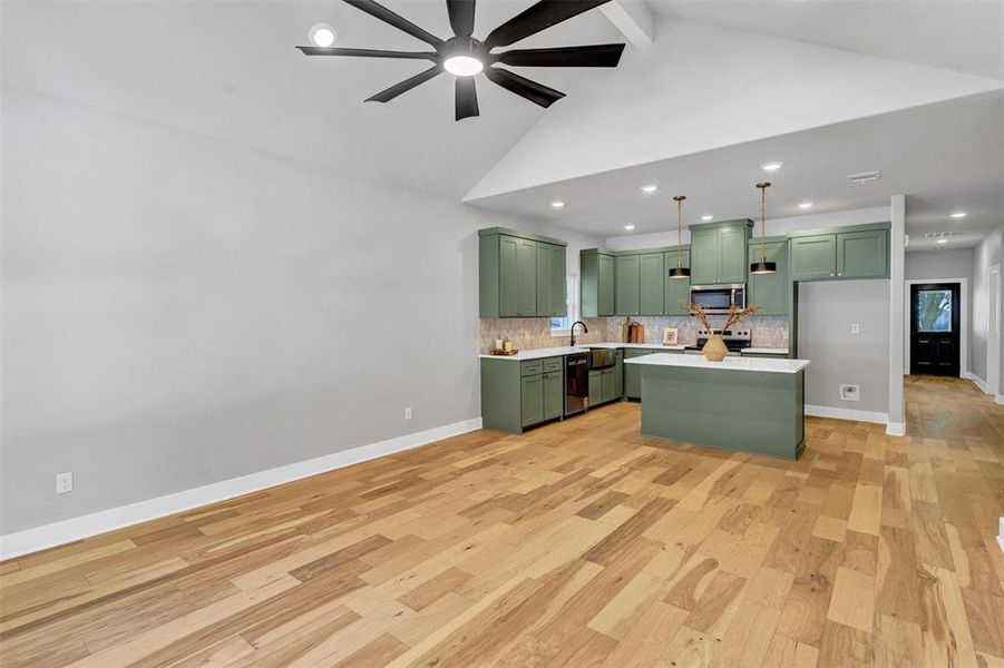 Kitchen featuring green cabinets, a kitchen island, light wood-type flooring, hanging light fixtures, and beamed ceiling