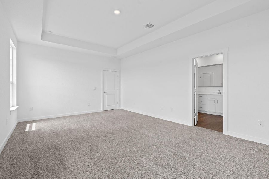 Unfurnished bedroom with carpet flooring, a raised ceiling, and connected bathroom Unfurnished bedroom with carpet flooring, a raised ceiling, and connected bathroom