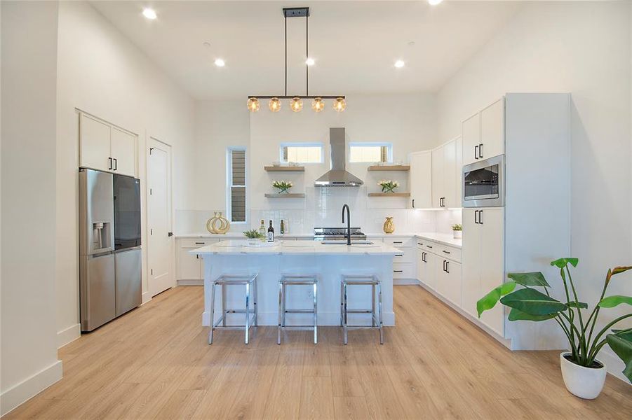 Kitchen with decorative light fixtures, stainless steel appliances, backsplash, white cabinetry, and a center island with sink Kitchen with decorative light fixtures, stainless steel appliances, backsplash, white cabinetry, and a center island with sink