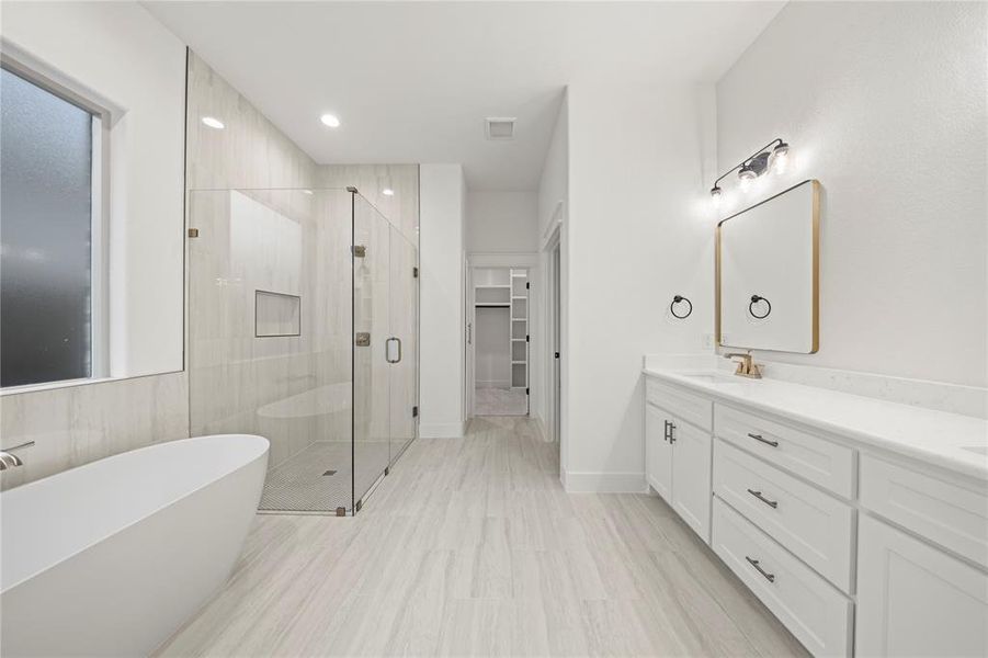 Full bathroom featuring a freestanding tub, double vanity, a stall shower, a walk in closet, and recessed lighting