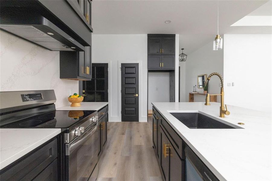 Kitchen featuring stainless steel appliances, sink, wall chimney range hood, light hardwood / wood-style floors, and hanging light fixtures