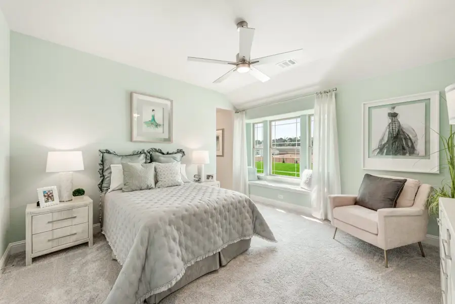 Bedroom with vaulted ceiling, ceiling fan, window seat, and light green walls with carpet flooring
