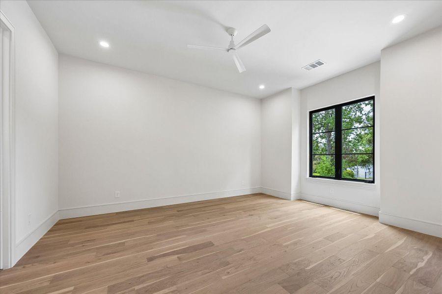 Wide plank wood floors, and oversized black framed windows create a bright, inviting secondary bedroom. An attached ensuite bath provides comfort and privacy for family members or overnight guests.